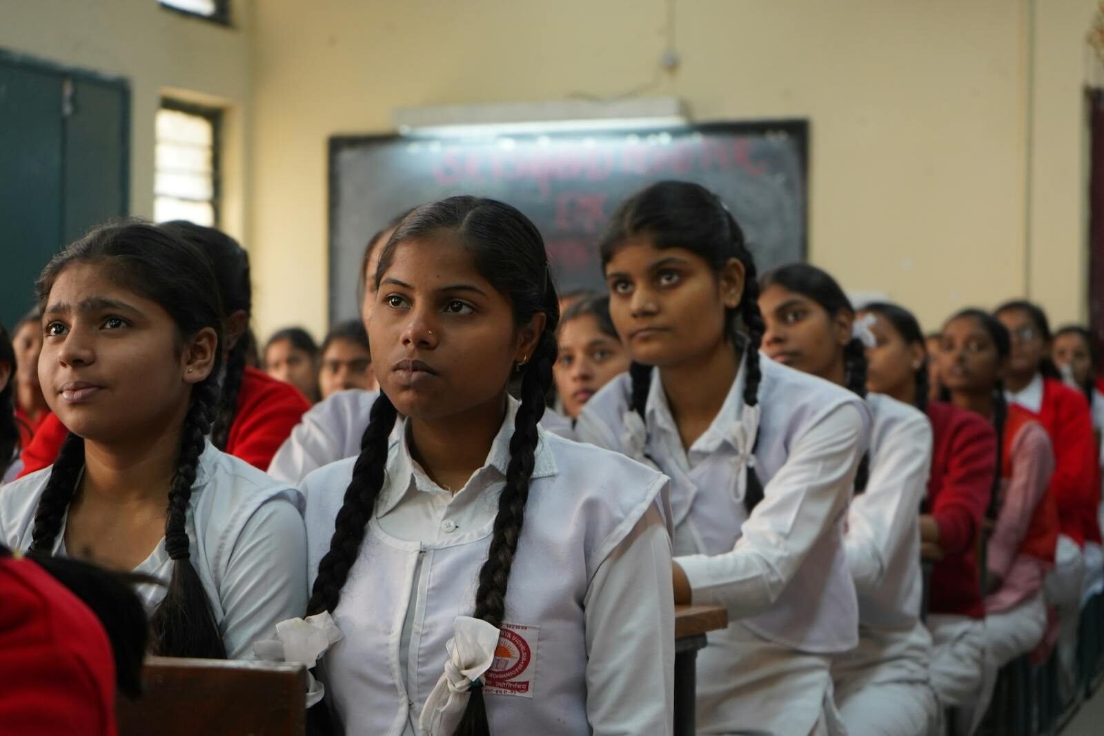 Group of Indian schoolgirls attentively listening in their classroom wearing uniforms.