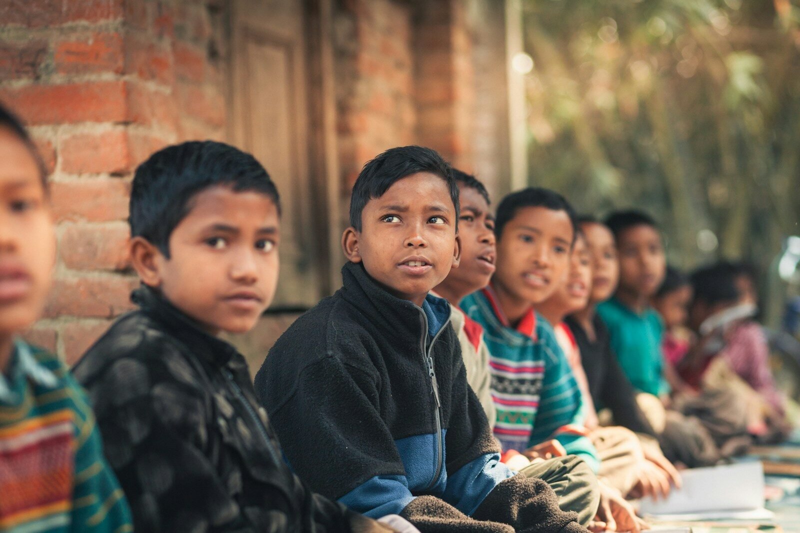 A group of children sitting in a line outdoors.